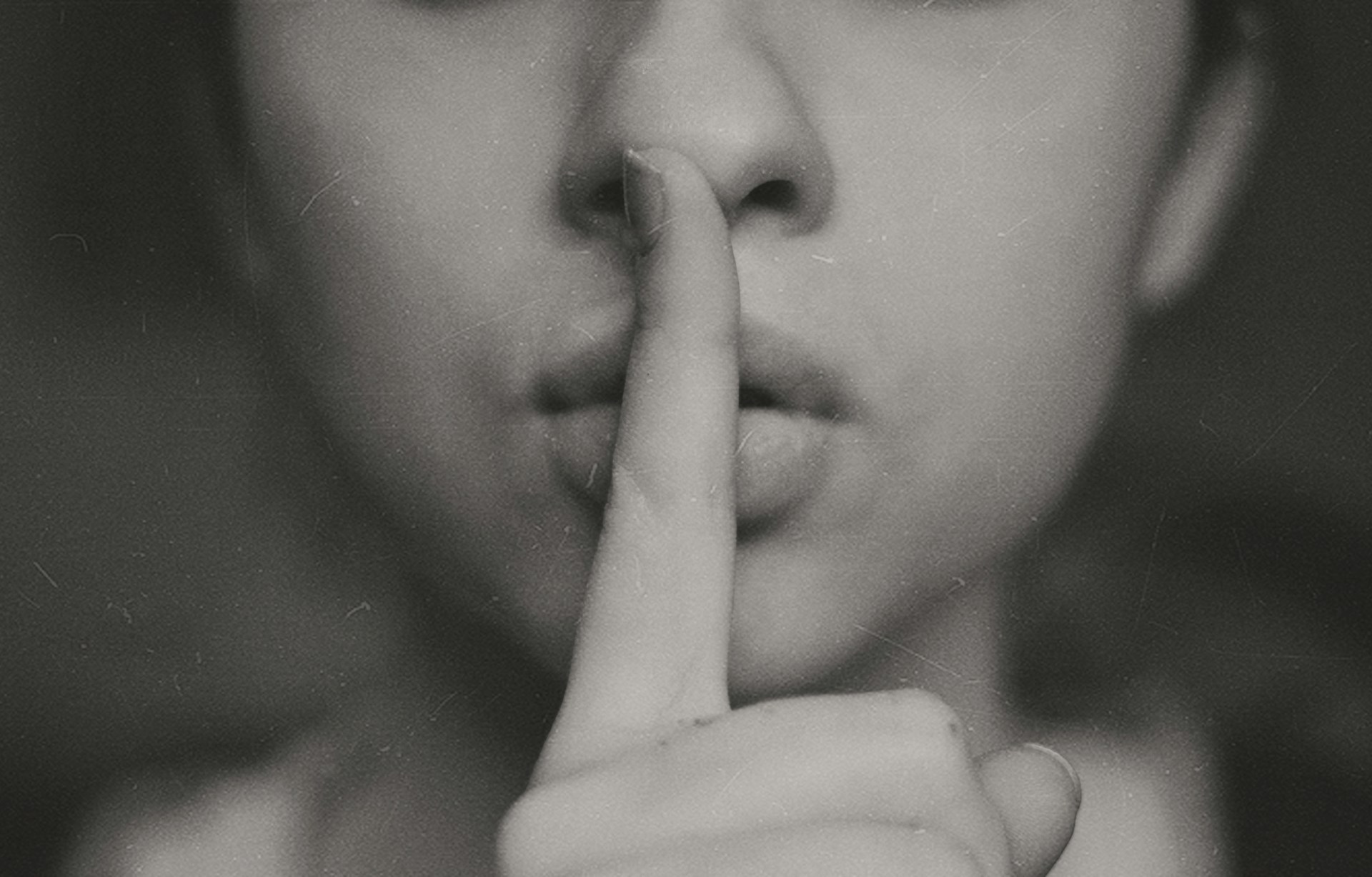 Description: grayscale photo of woman doing 'shhh' motion with finger across her lips. Photo by Kristina Flour on Unsplash.