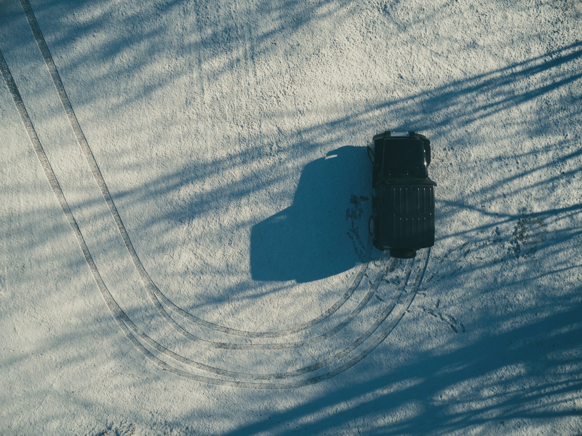 Overhead shot of a car in the snow. The tire tracks indicate that the car has done a u-turn. Photo by Ozark Drones on Unsplash.