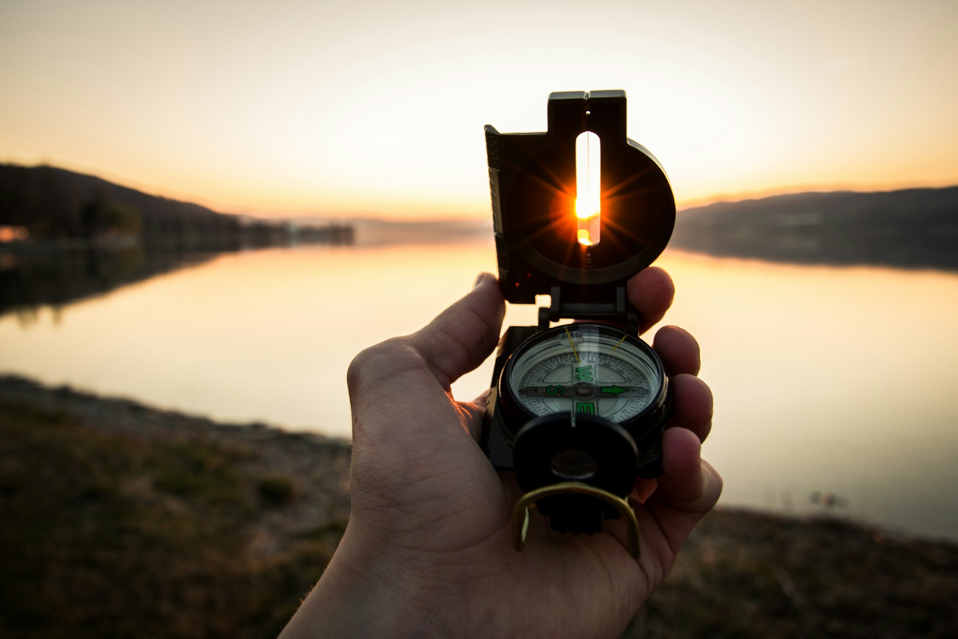 A hand holding an open compass.  The sun shines through a slit in the compass cover.