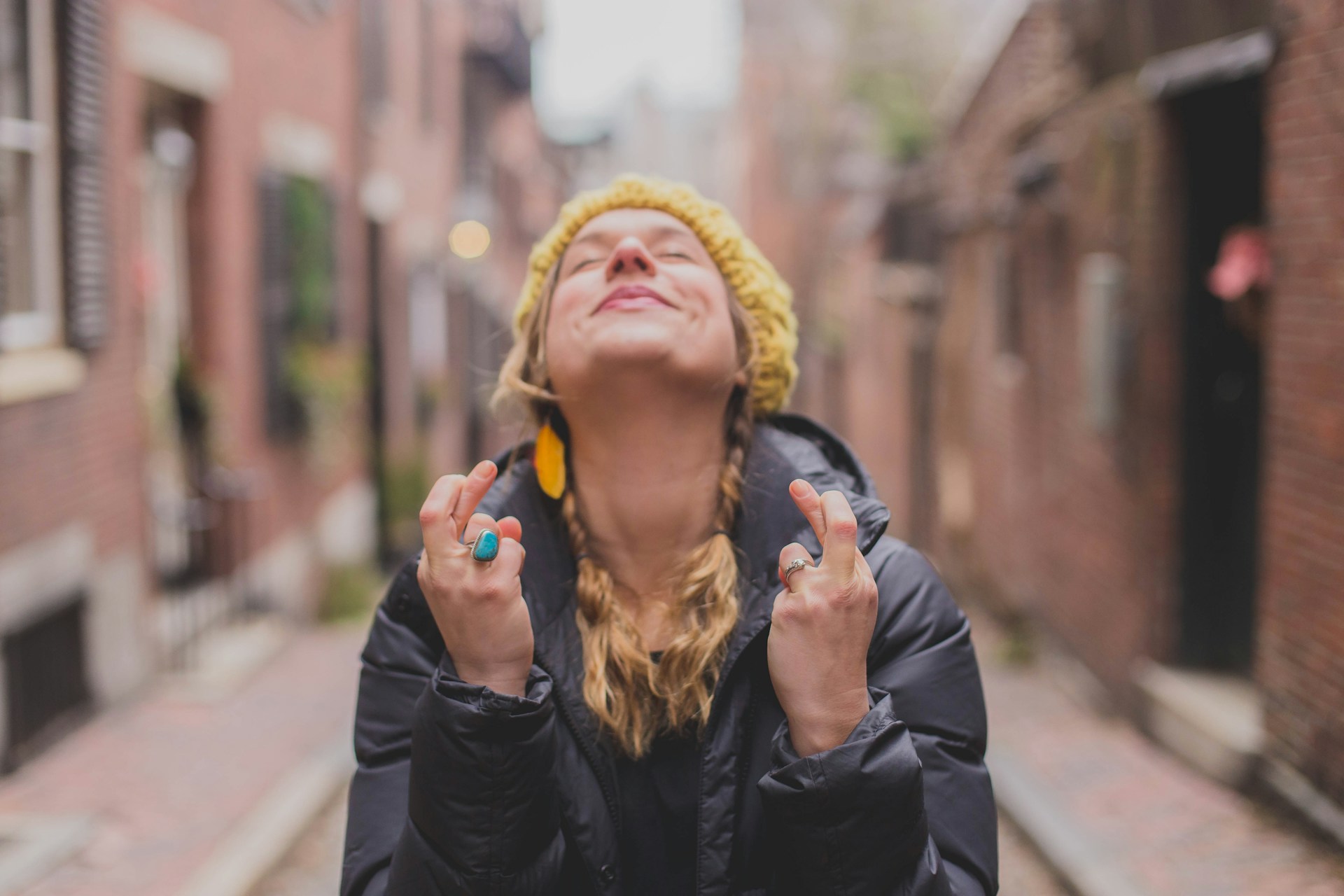 A woman, eyes closed, crossing her fingers and facing the sky (as though she is wishing very hard for something). Photo by Dayne Topkin on Unsplash