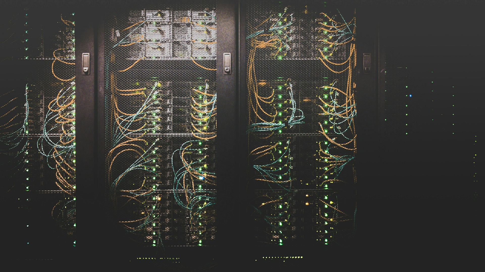 A wall of racked machines in a server room cage.  Three cages are well-lit; the fourth is dim.  Photo by Taylor Vick on Unsplash