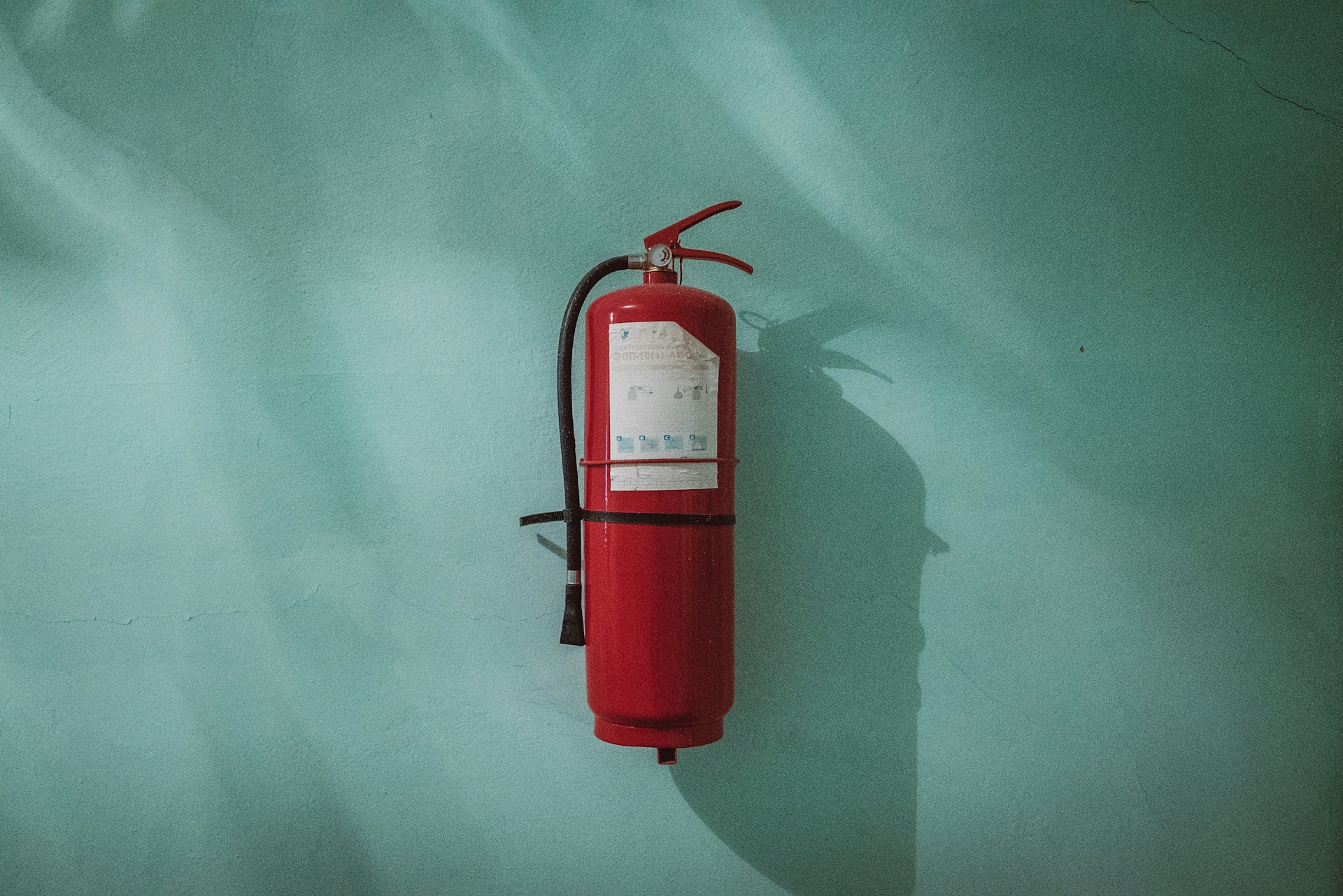 A red fire extinguisher on a light-blue background.   Photo by Piotr Chrobot on Unsplash.