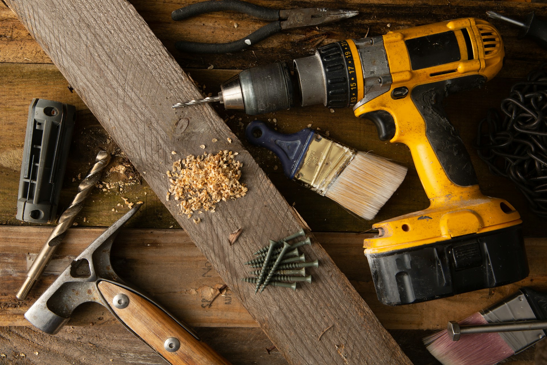 A drill, screws, and assorted tools next to a plank of wood.   Photo by benjamin lehman on Unsplash.