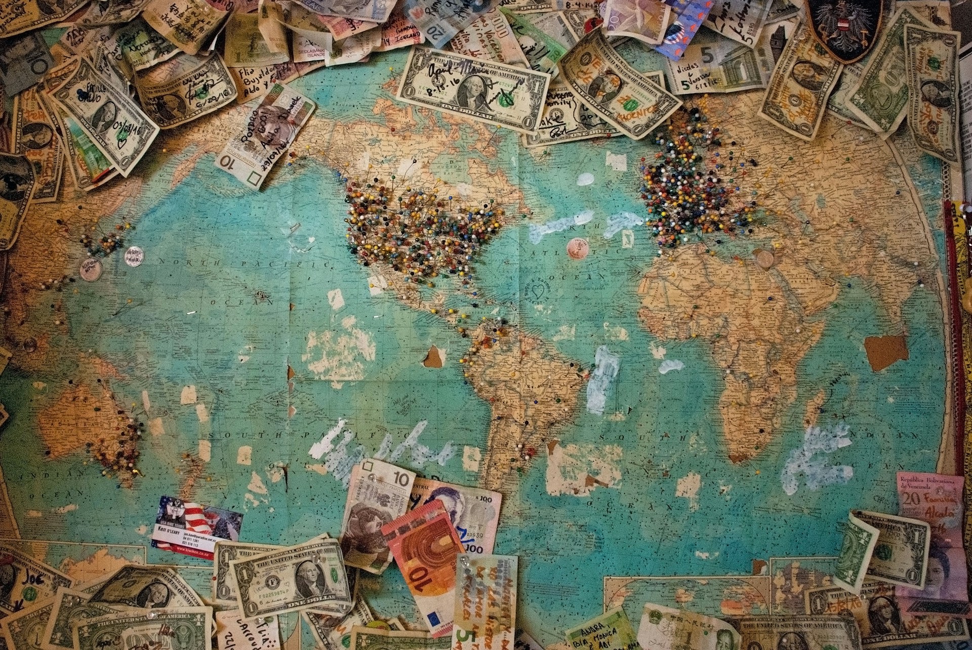 A world map with currency scattered around the edges.   Photo by Christine Roy on Unsplash.