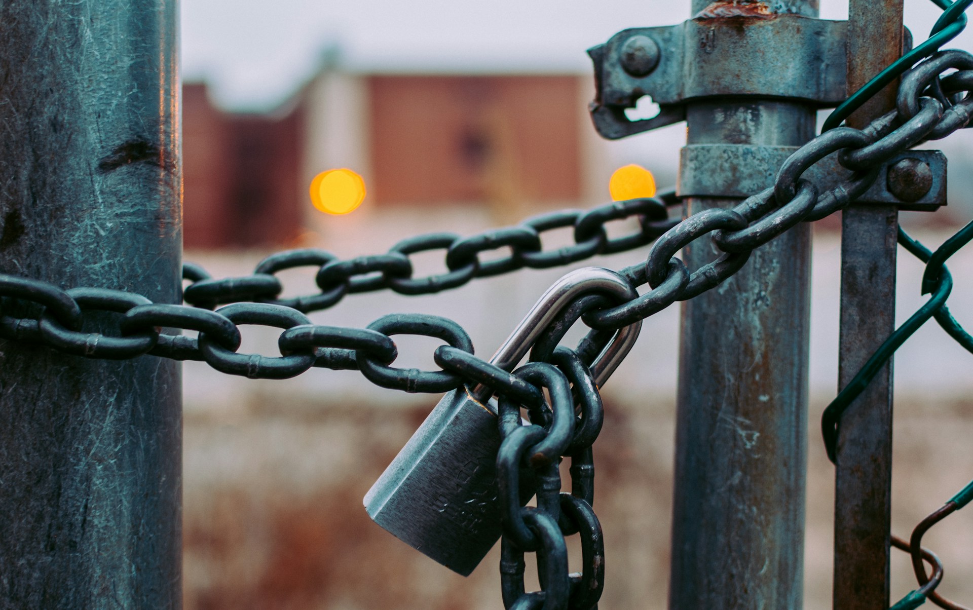 A padlock, attached to a chain that is holding a gate closed. Photo by Jose Fontano on Unsplash.