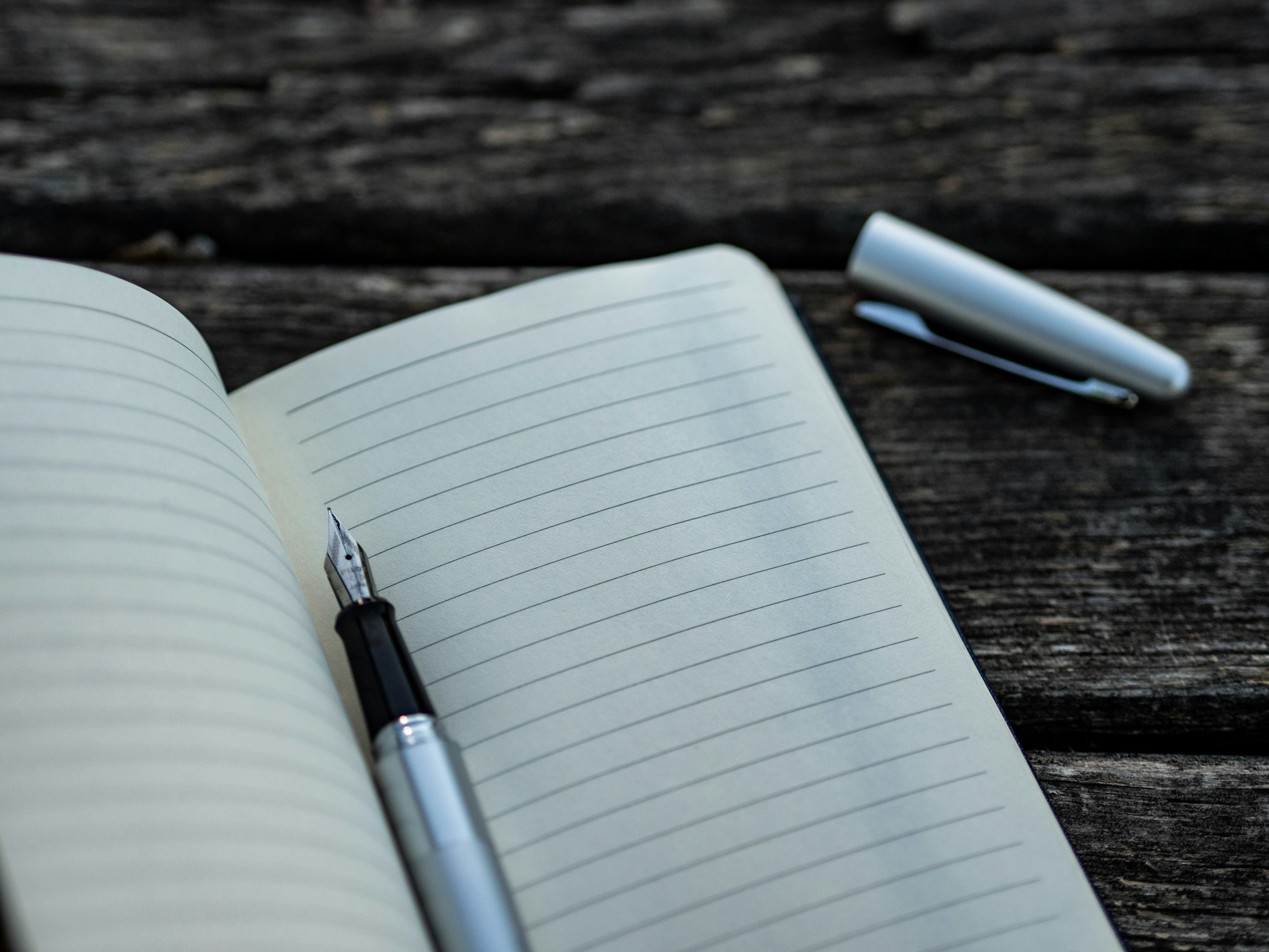 A fountain pen resting on the pages of an open notebook.  The pages are blank.   Photo by Aaron Burden on Unsplash.