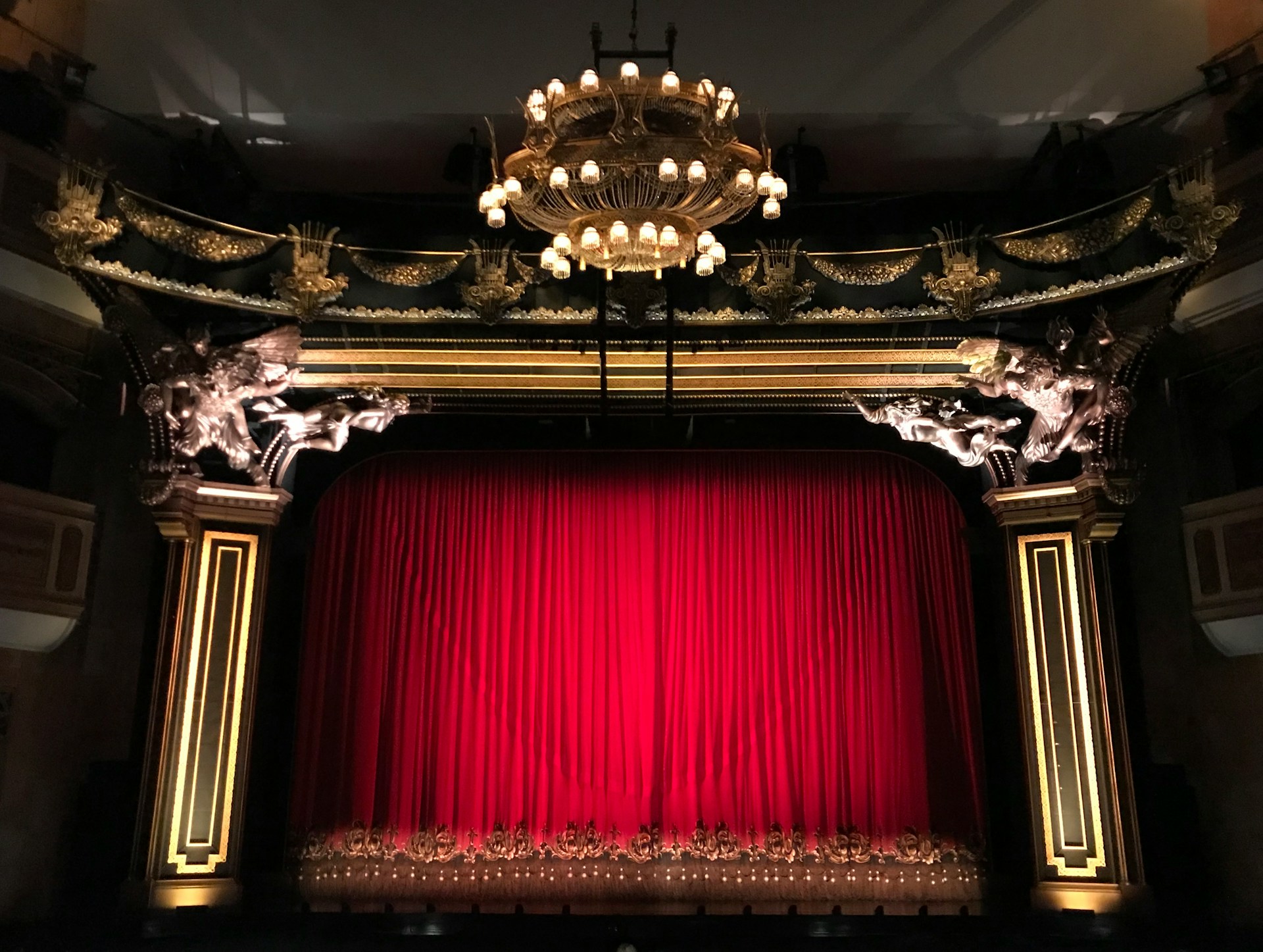 A long shot of a stage, with red curtains.  Photo by Gwen King on Unsplash.