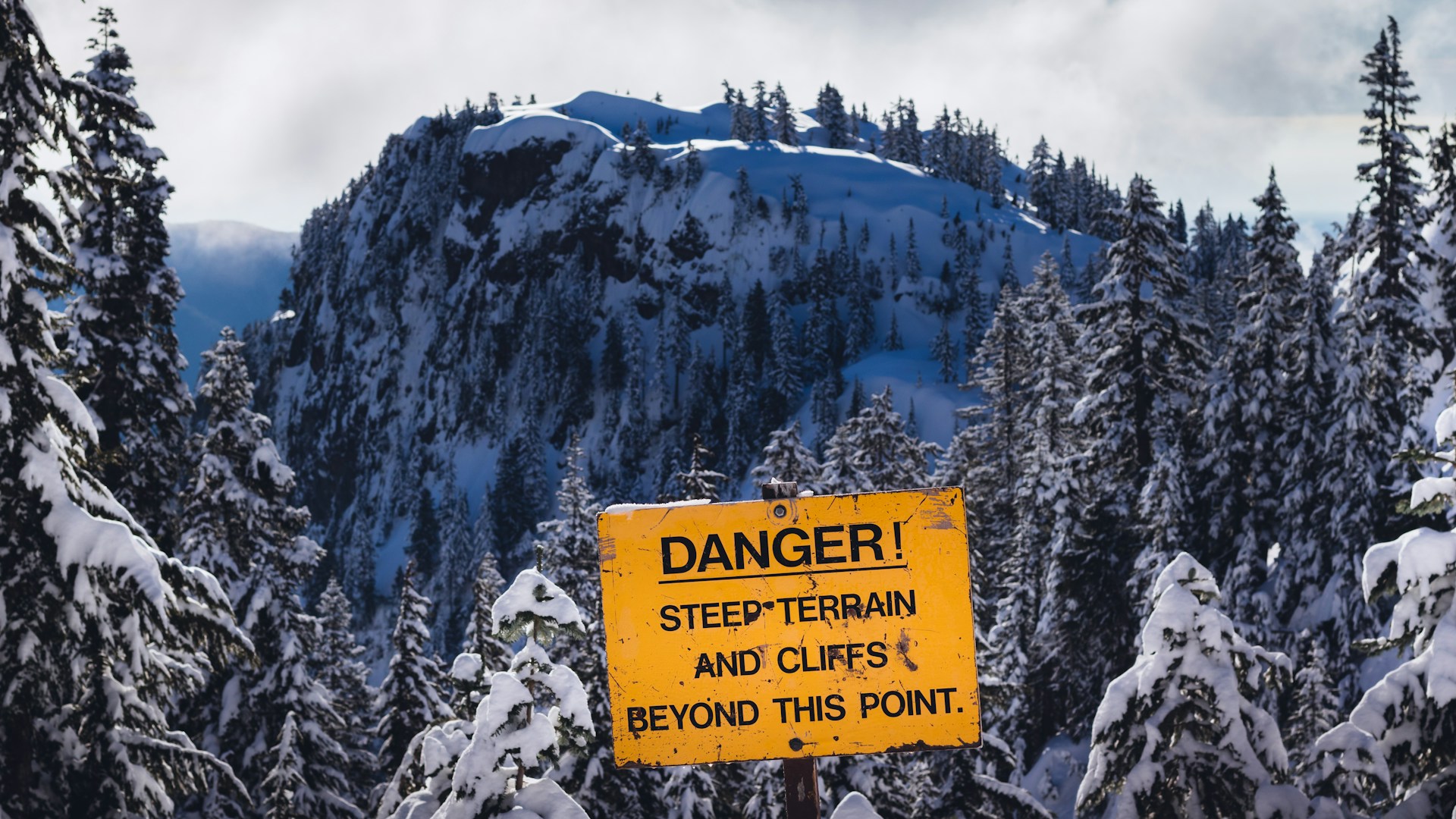 A sign that reads 'Danger: steep terrain and cliffs beyond this point'. Photo by Greg Rosenke on Unsplash.