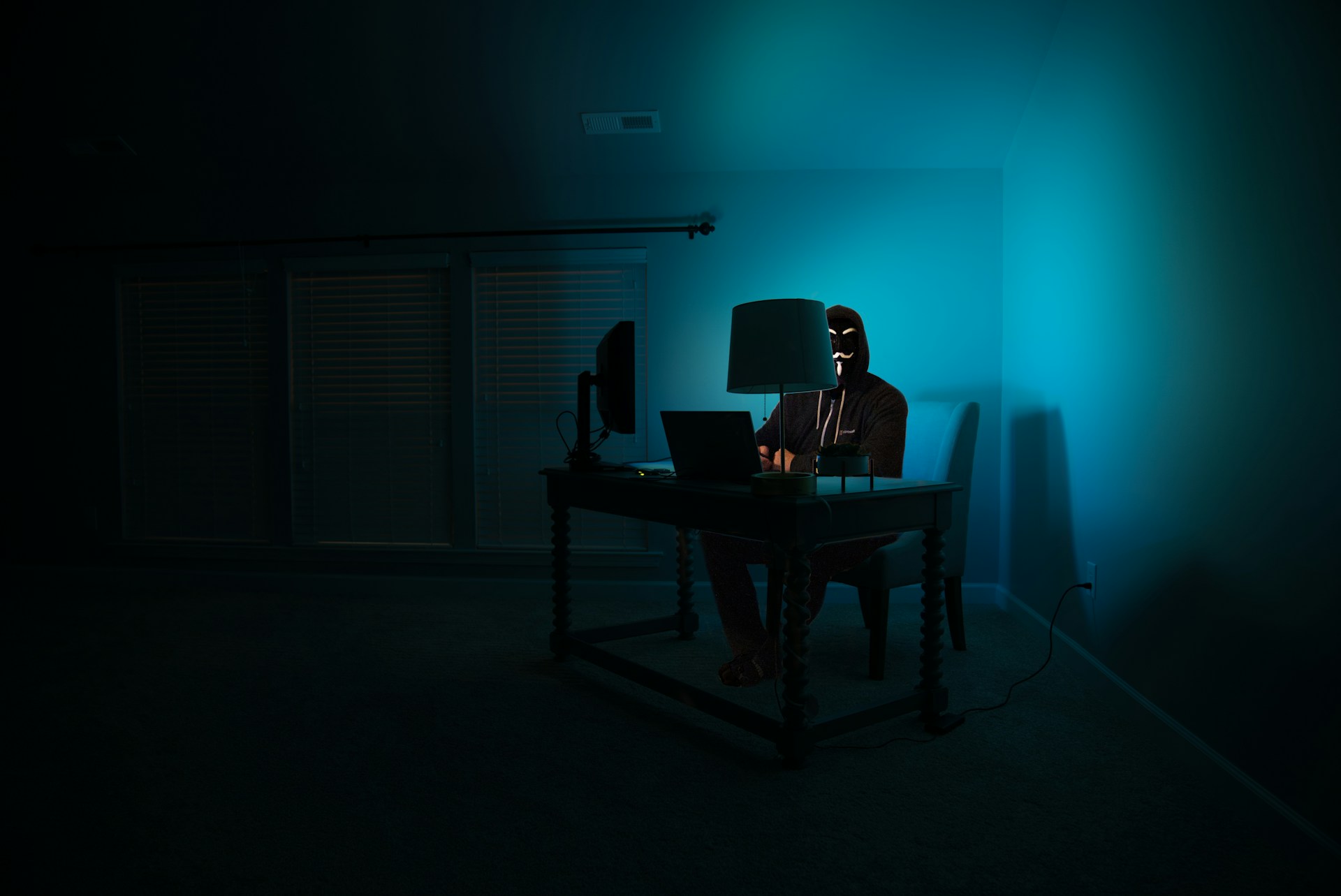 A person in front of a computer, disguised as an Anonymous hacker wearing a Guy Fawkes mask.  Photo by Clint Patterson on Unsplash
