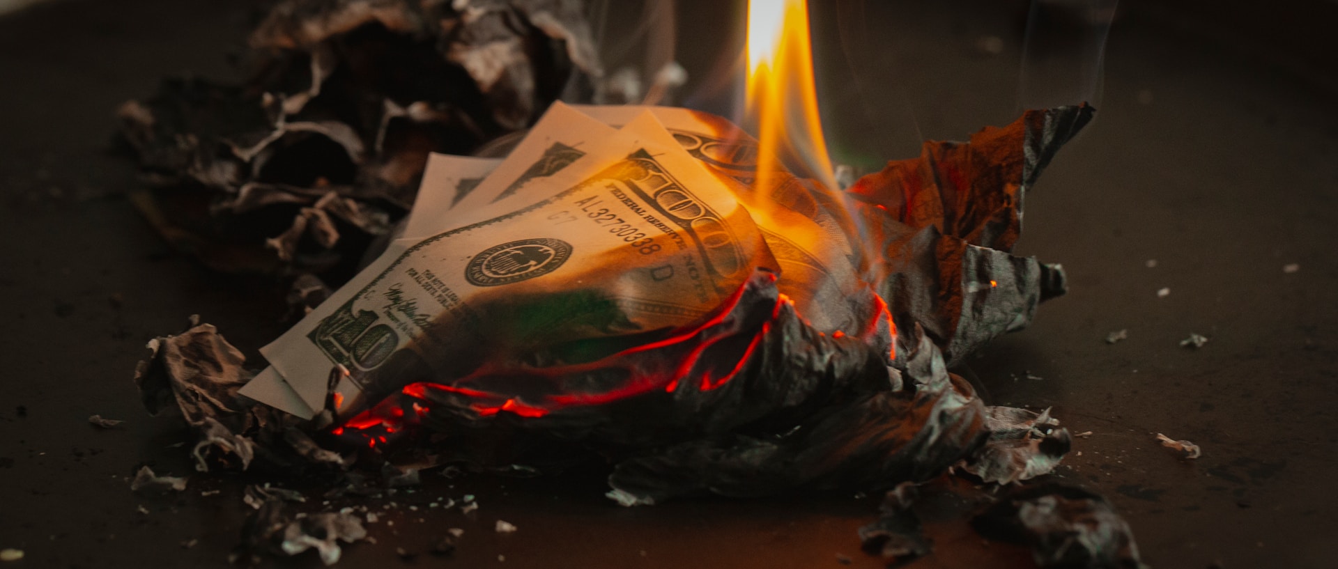 A hand holding dollar bills that are on fire.