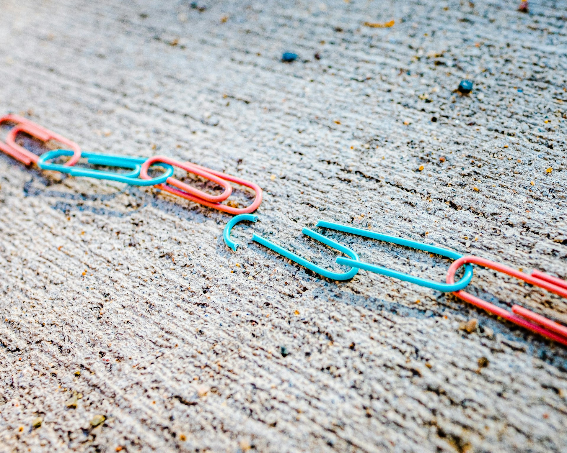 A chain made of colorful paperclips. Two paperclips in the center are broken. Photo by Jackson Simmer on Unsplash.