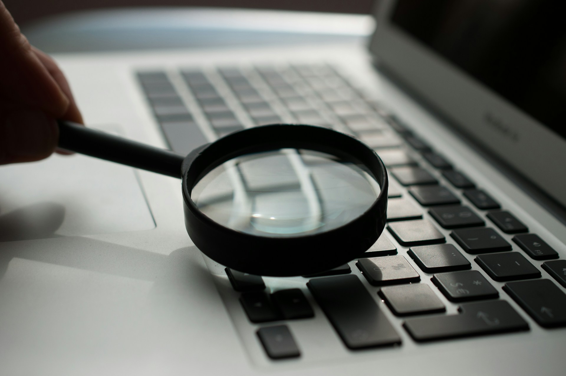 A magnifying glass held over a laptop keyboard, as though someone is inspecting the computer.  Photo by Agence Olloweb on Unsplash.