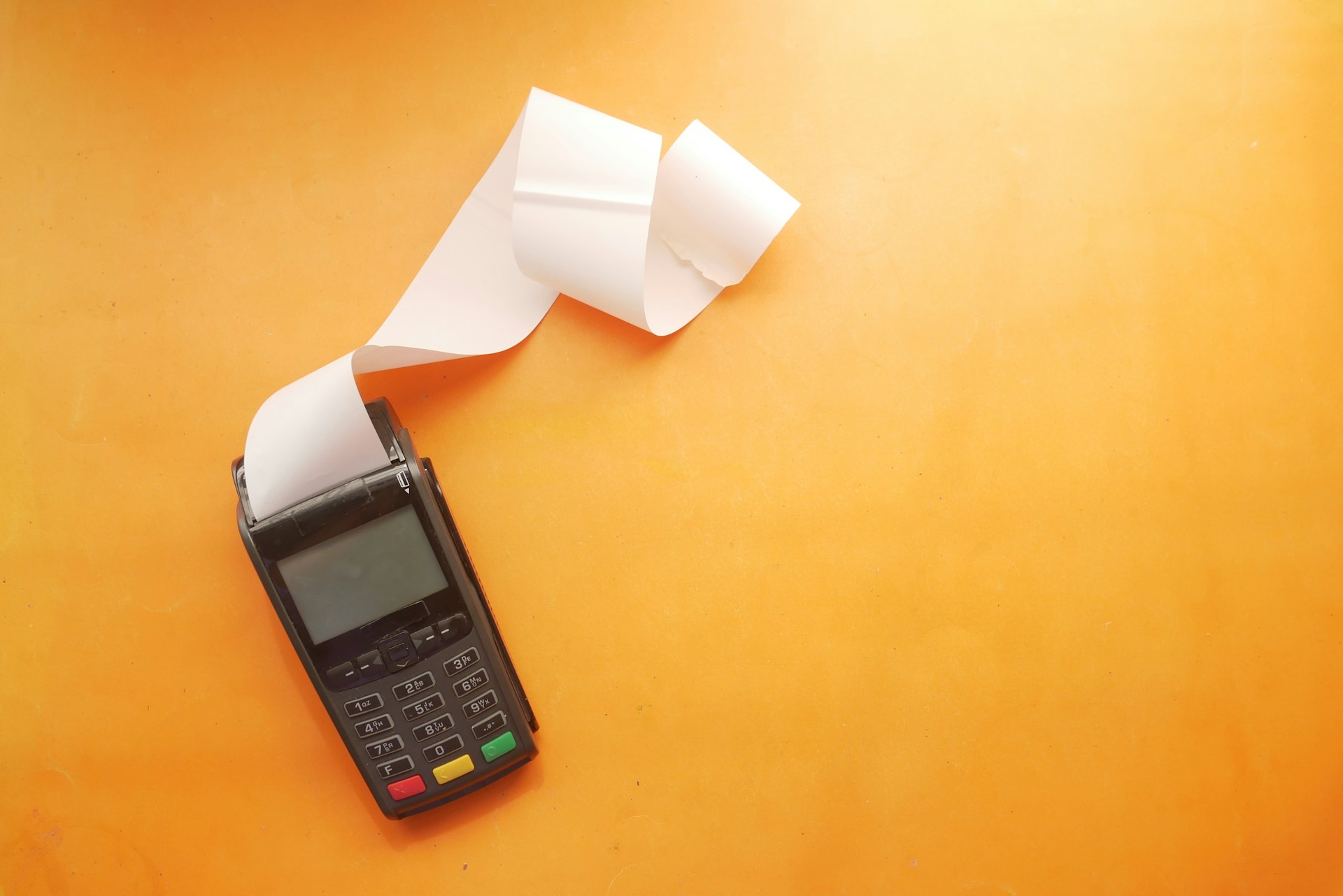 A handheld card-reader with a long receipt printing out of it. Photo by Towfiqu barbhuiya on Unsplash.