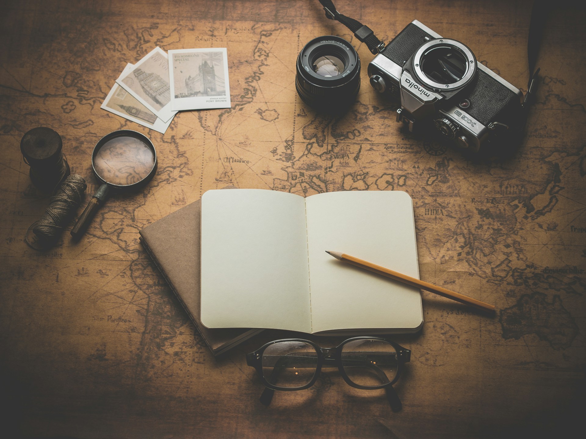An open, blank notebook with glasses and a camera, all sitting on a map.  Photo by Dariusz Sankowski on Unsplash.
