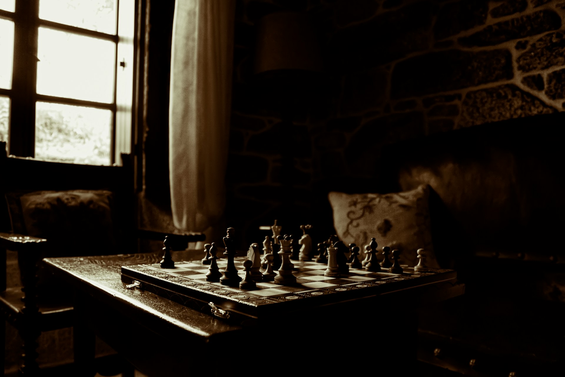 A chessboard on a table beside a window.  Photo by Javier Grixo on Unsplash.