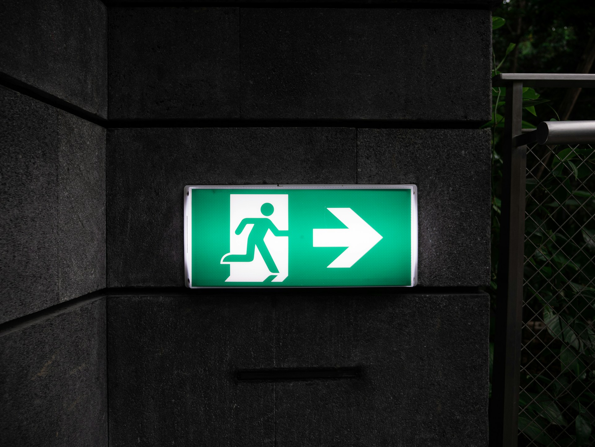 A green 'exit' sign on a dark background.  Photo by Andrew Teoh on Unsplash.